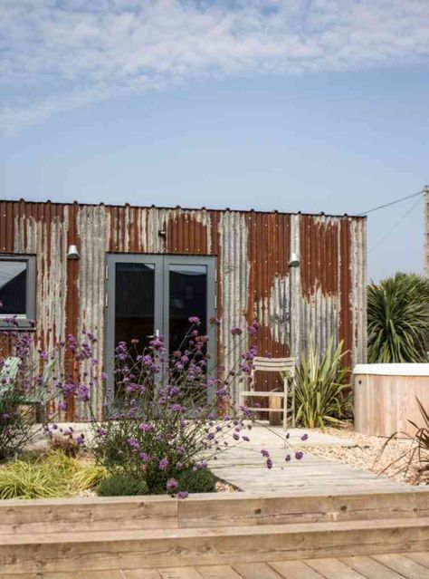 a building made out of old corrugated sheets with plants and flowers in the foreground