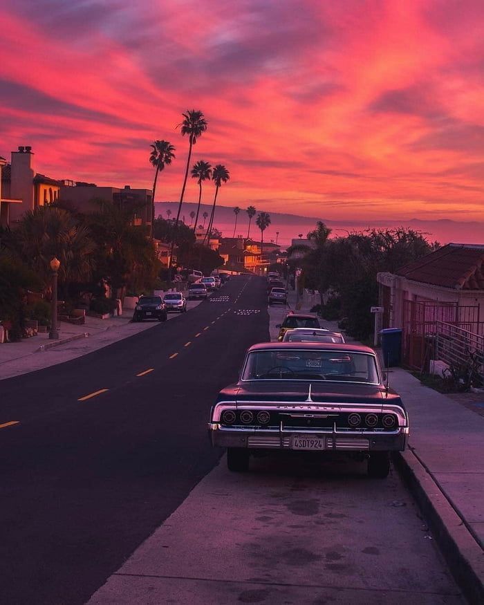 an old car is parked on the side of the road as the sun goes down