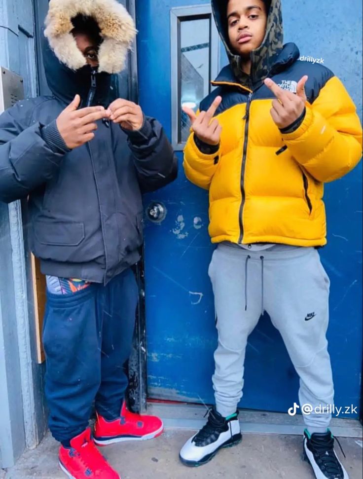 two young men standing next to each other in front of a blue door wearing winter clothes