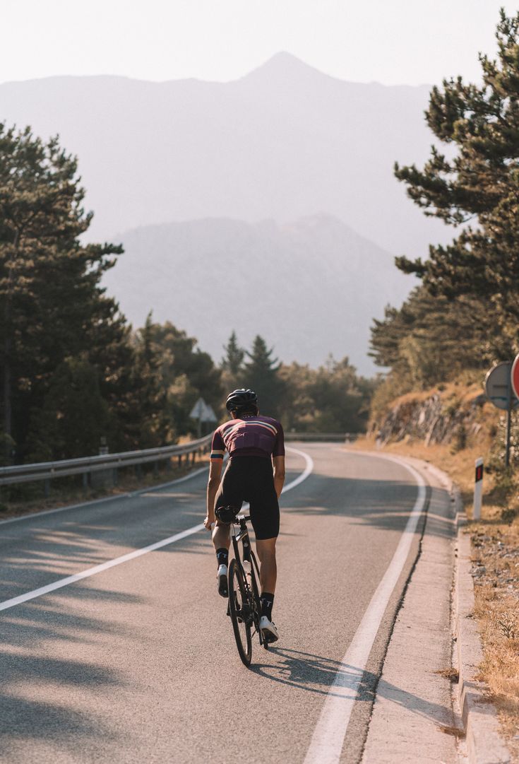 a bicyclist rides down the road in front of some trees and mountains