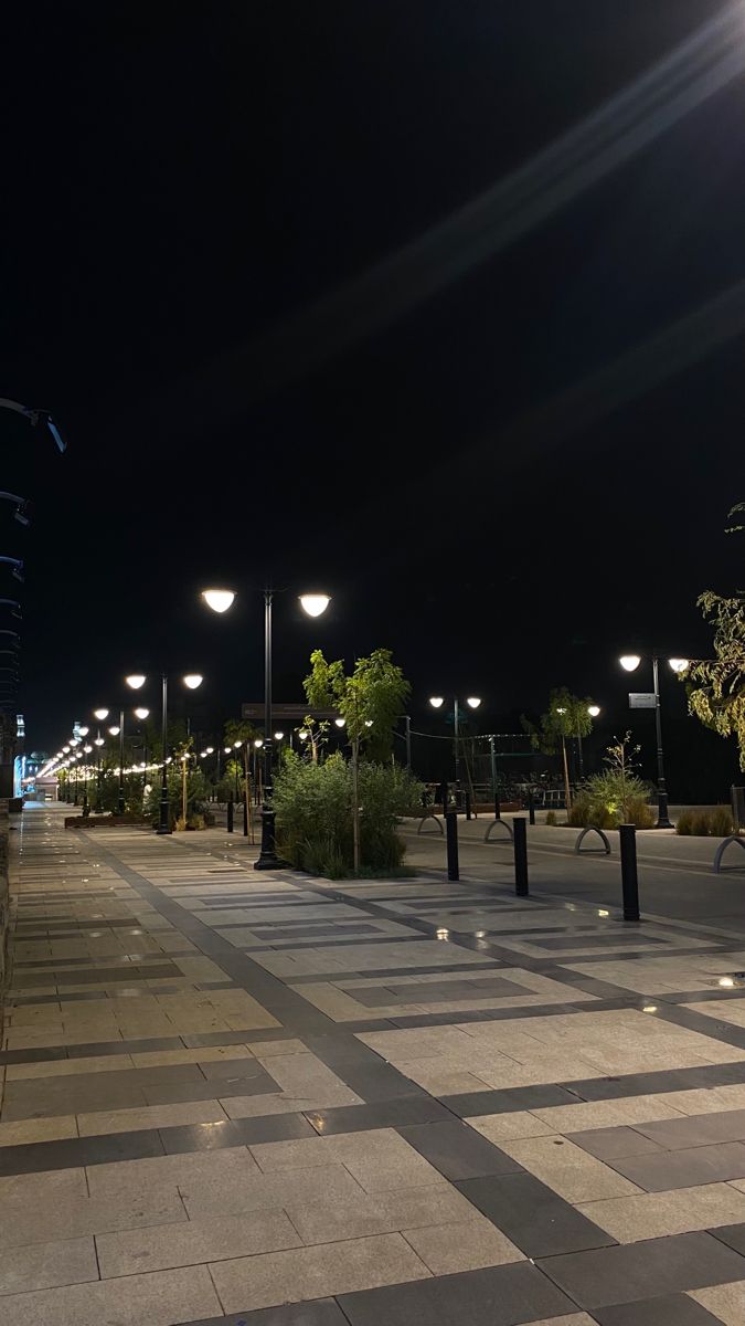 an empty sidewalk at night with street lights