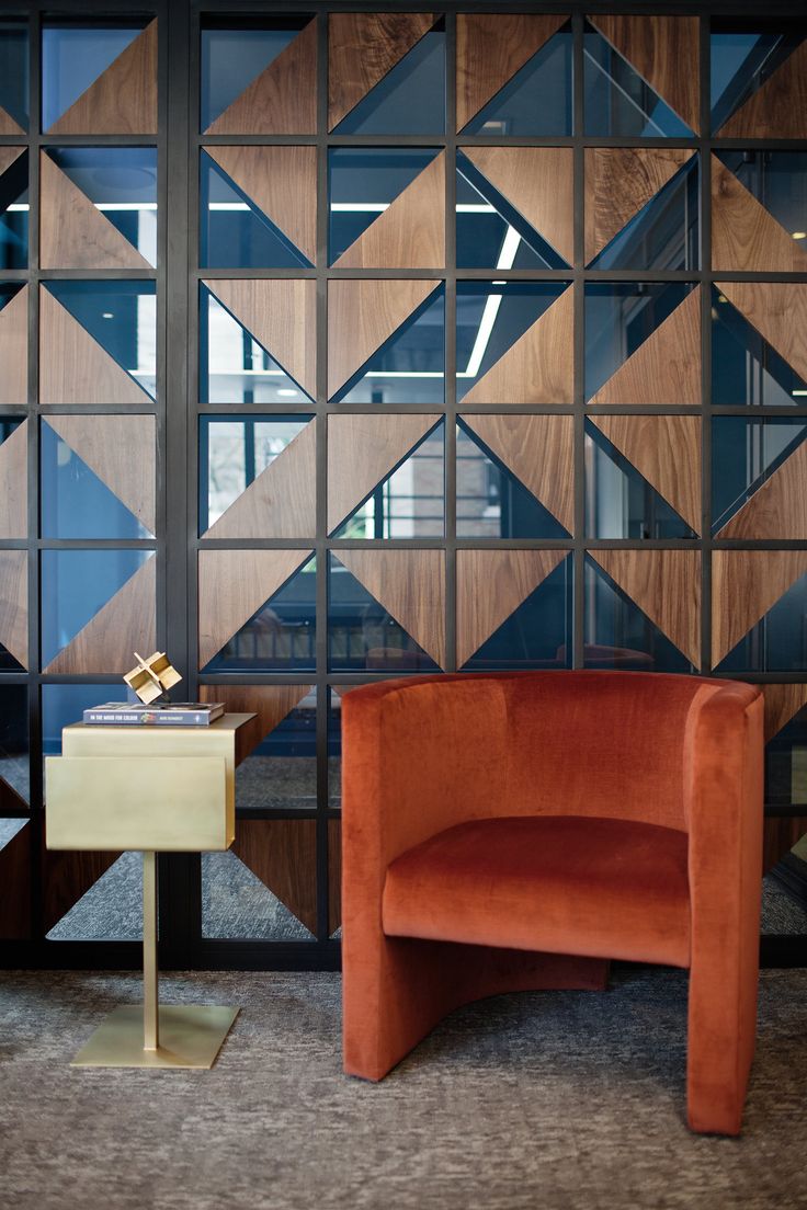 an orange chair sitting in front of a wooden wall with geometric designs on it's sides