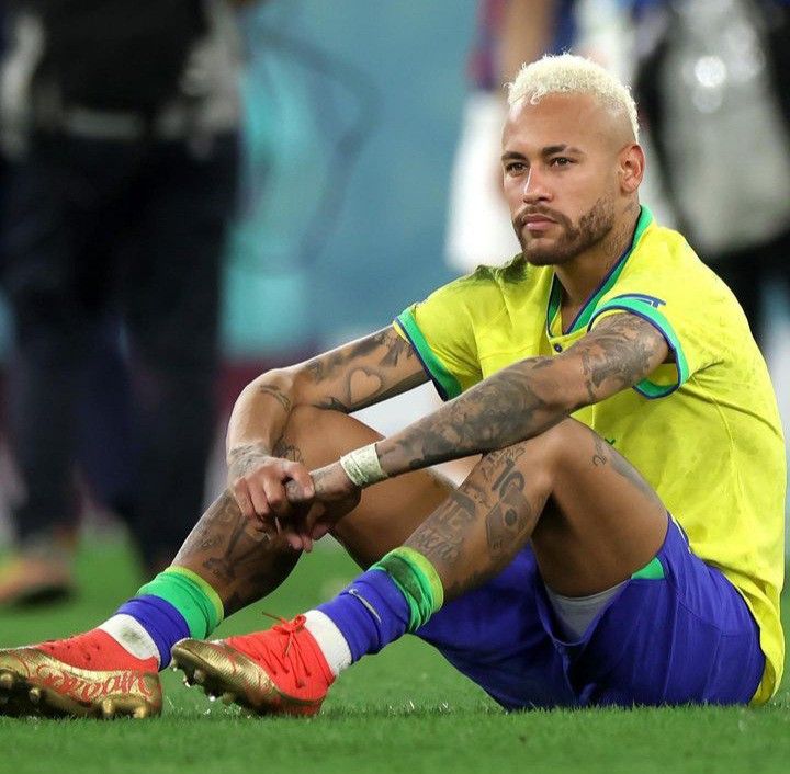 a soccer player sitting on the ground with his legs crossed and hands behind his head