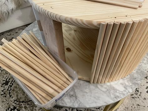 a round table made out of wood sticks on a marble top with a clear plastic container next to it