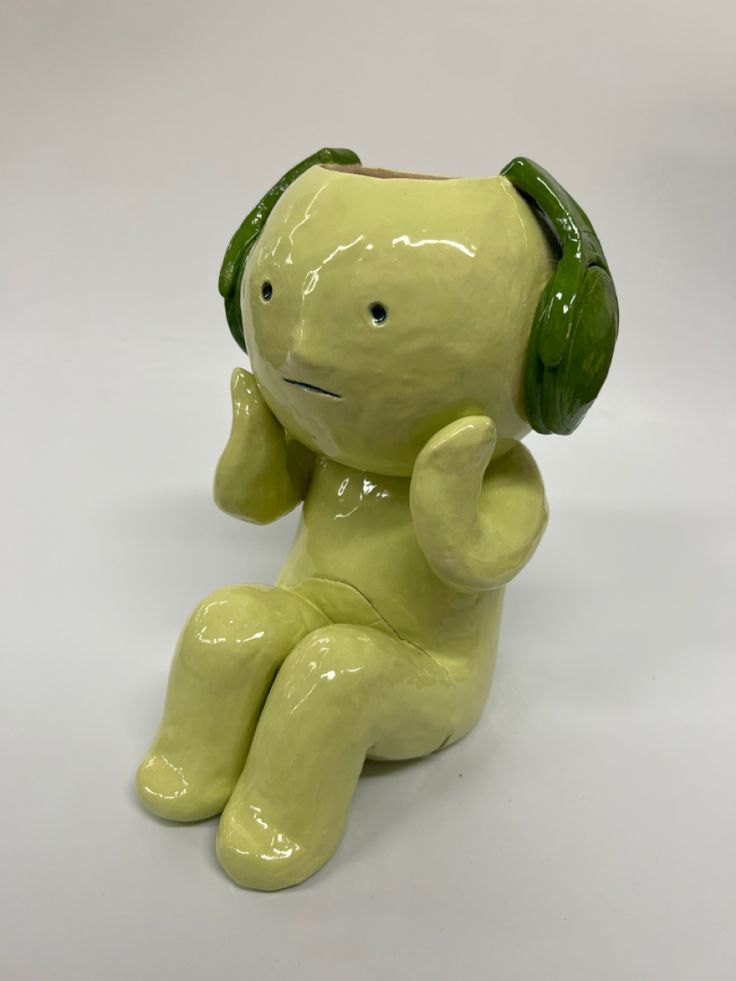 a yellow ceramic elephant with headphones on its ears sitting in front of a white background