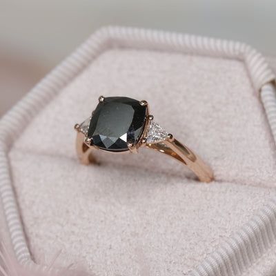 a black diamond ring sitting on top of a white cloth covered cushioned box with its lid open