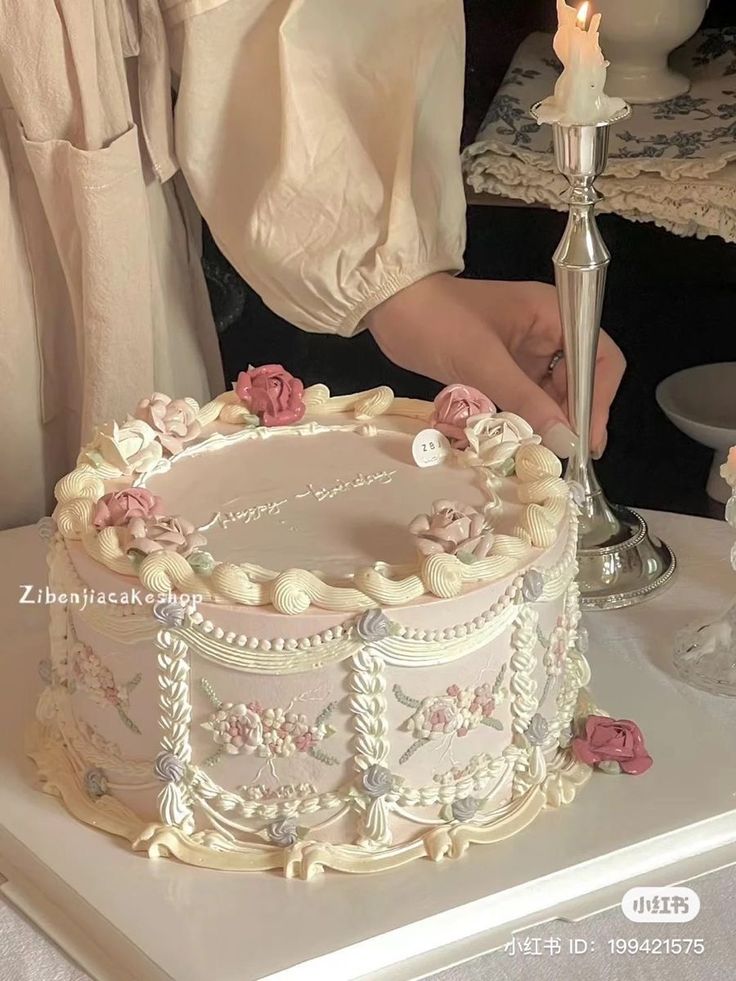 a woman is decorating a cake with white frosting and pink flowers on it