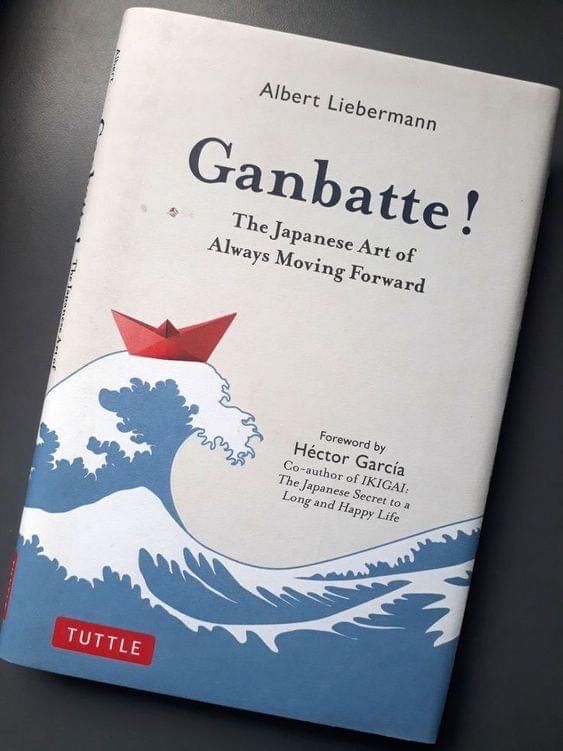 an open book with a red paper boat floating on top of the ocean and it says, ganbate