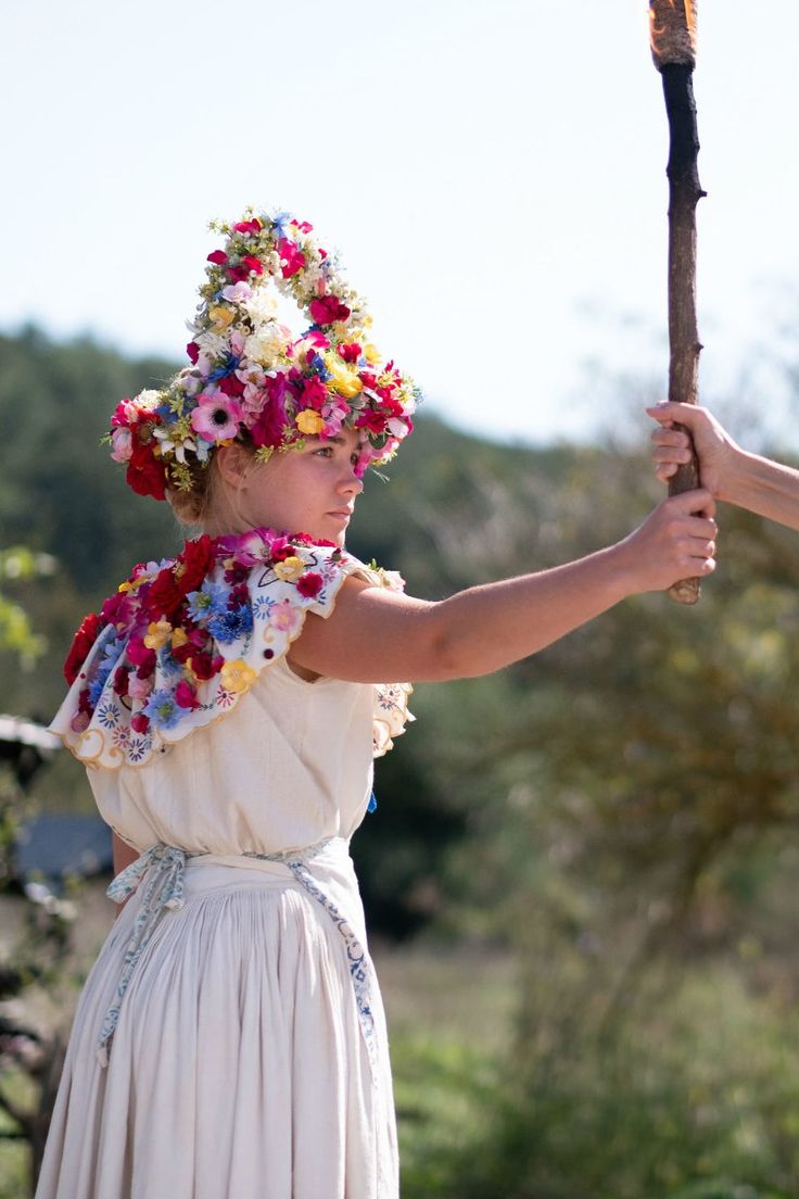 a woman in a white dress holding a stick and wearing a flowered headdress