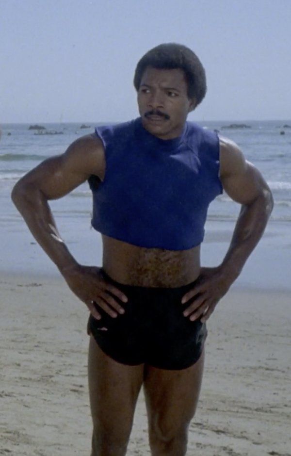 a man standing on top of a sandy beach next to the ocean with his hands on his hips