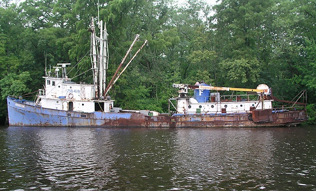 an old rusted boat sitting in the middle of a body of water near some trees