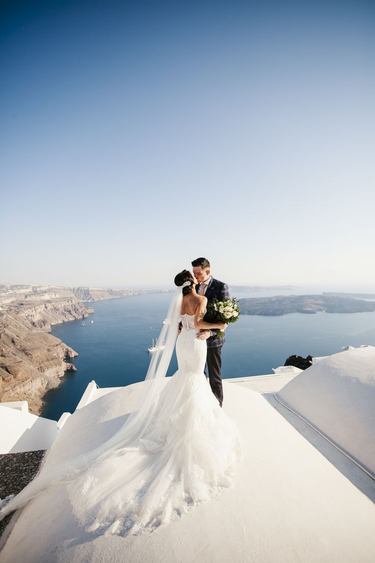 a bride and groom standing on top of a snow covered hill with the ocean in the background