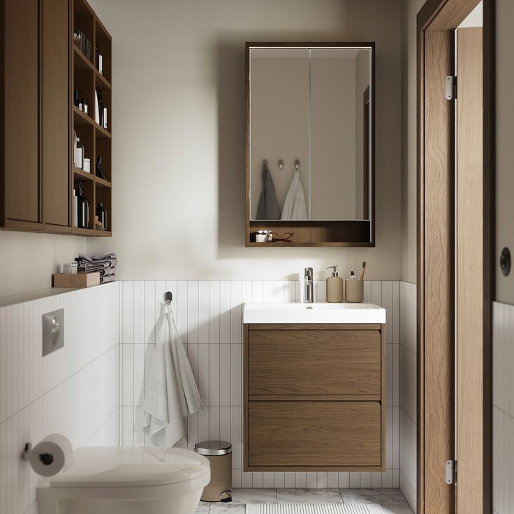 a white toilet sitting next to a bathroom sink under a mirror above a wooden cabinet