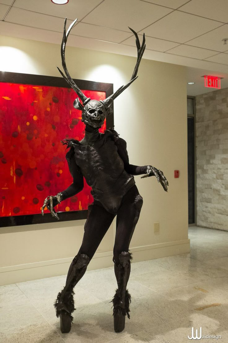 a woman dressed as a creature in front of a large red and black painting on the wall