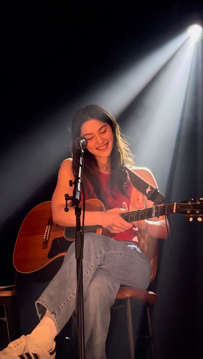 a woman sitting in front of a microphone and playing an acoustic guitar while singing into a microphone