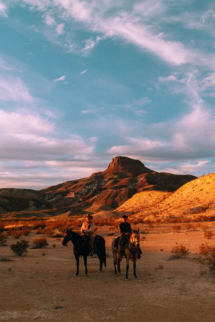 two people are riding horses in the desert with mountains in the backgrouds