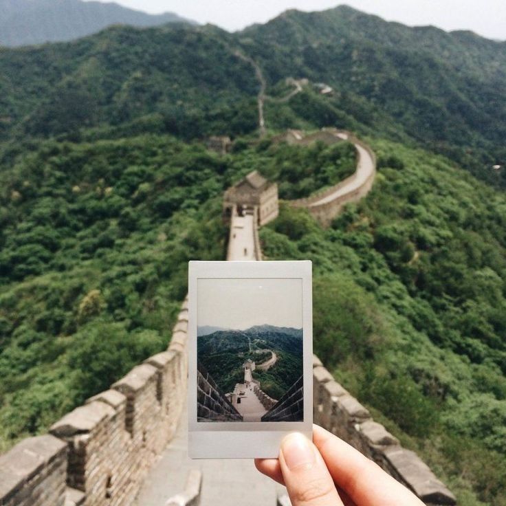 a person holding up a polaroid photo in front of the great wall of china