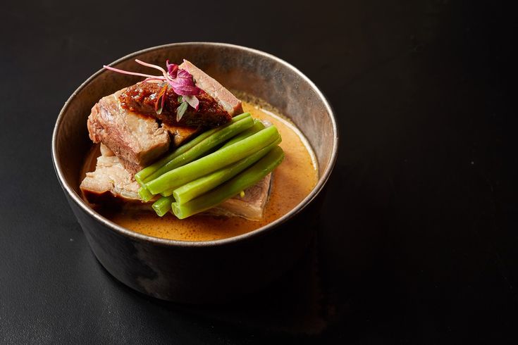 a bowl filled with meat and vegetables on top of a black table next to a spoon