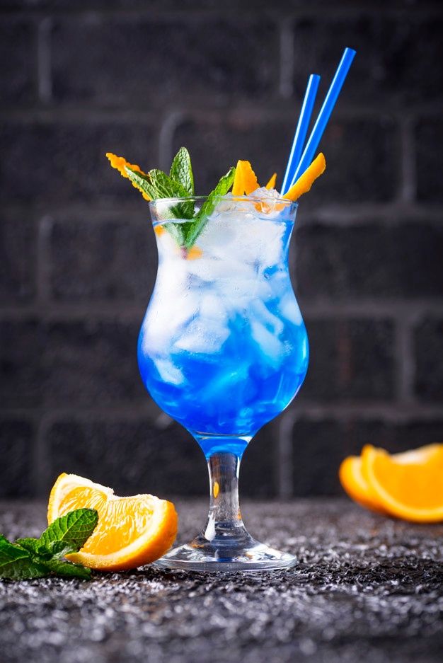 a blue drink with orange slices and mint garnish on the rim next to a brick wall