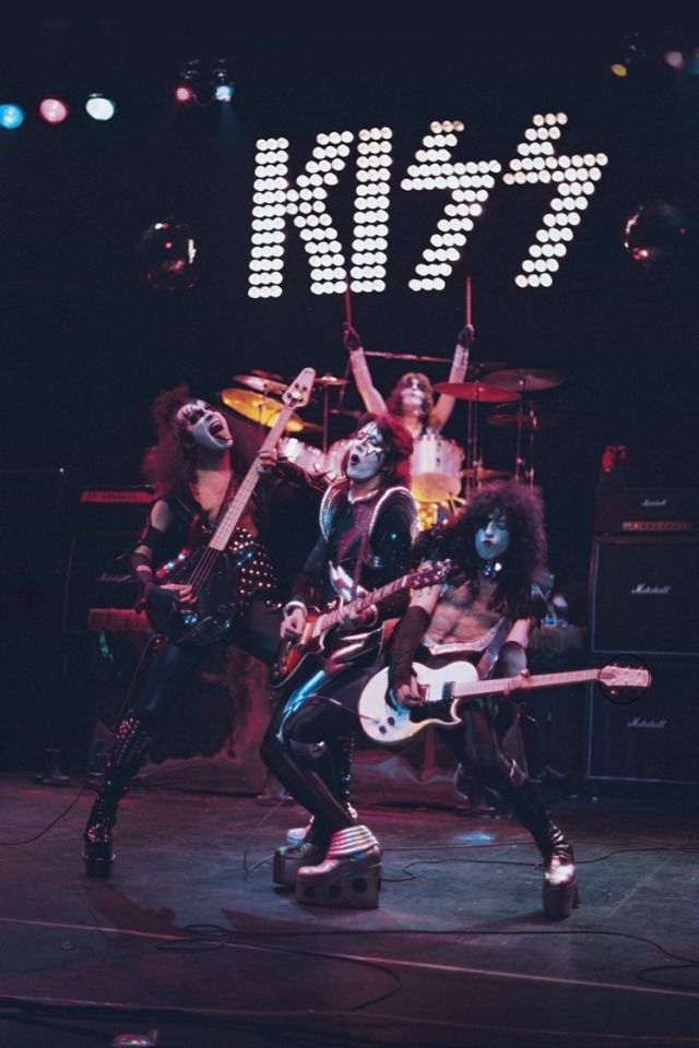 the kiss band performing on stage with their guitars in front of an advertisement for kiss