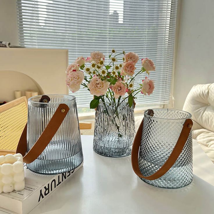 three vases with flowers in them sitting on a table next to a book and candle holder