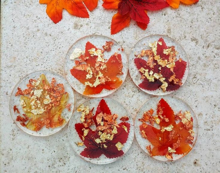 four glass plates with leaves on them sitting on a table next to autumn leaves and flowers