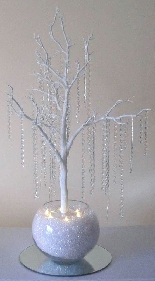 a white tree in a glass vase with lights on the branches and beads hanging from it