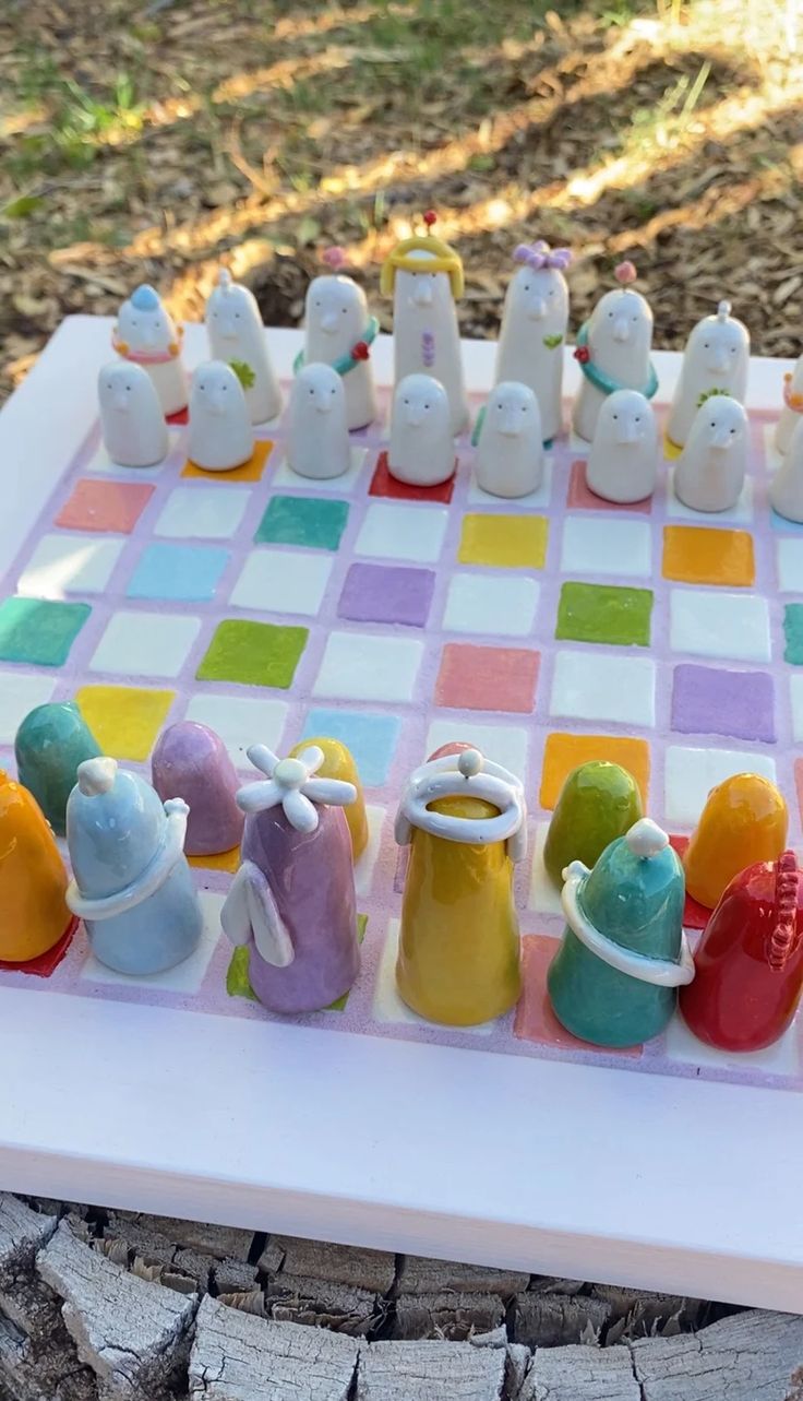 a colorful chess board with small figurines sitting on it's sides in front of a tree