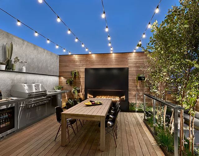 an outdoor kitchen and dining area is lit up with string lights, potted plants, and wood flooring