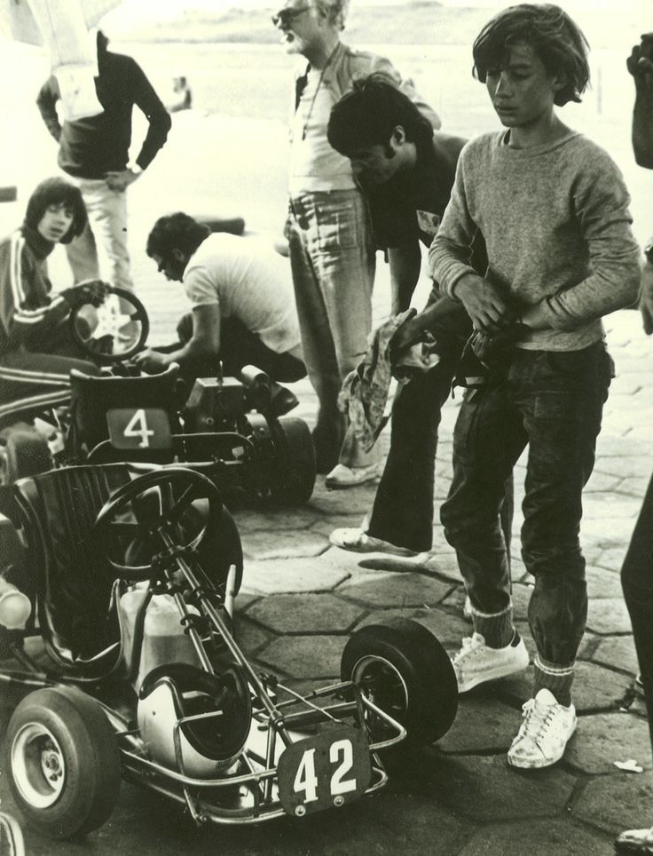 a group of young men standing next to each other near an old race car with the number 24 on it