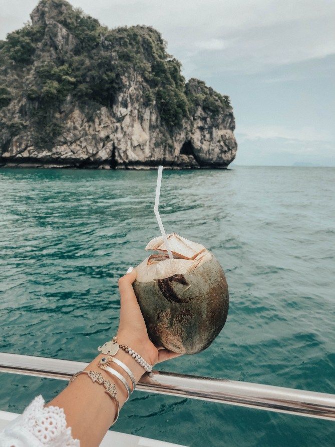 a hand holding a coconut on top of a boat near an island in the ocean