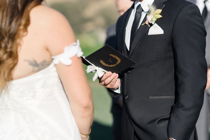 a man in a tuxedo is holding a book and standing next to a woman