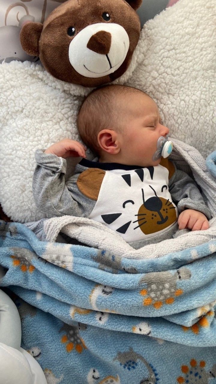 a baby laying on top of a blanket next to a teddy bear