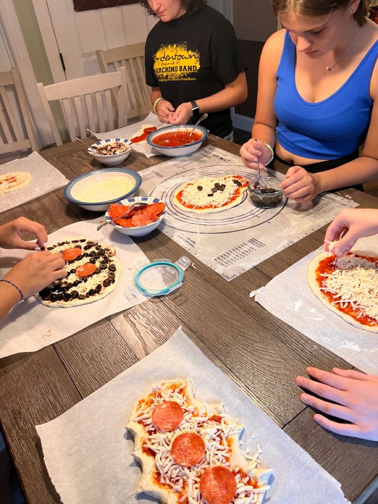 four people sitting at a table making pizzas