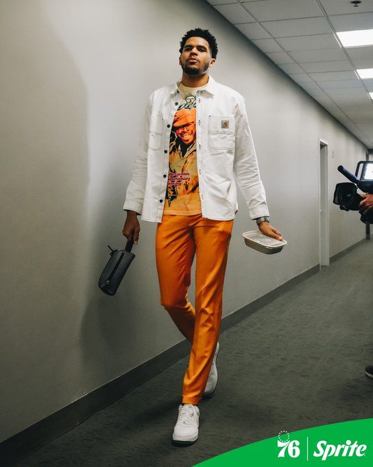 a man in an orange pants and white jacket walking down a hallway with his hand on his hip