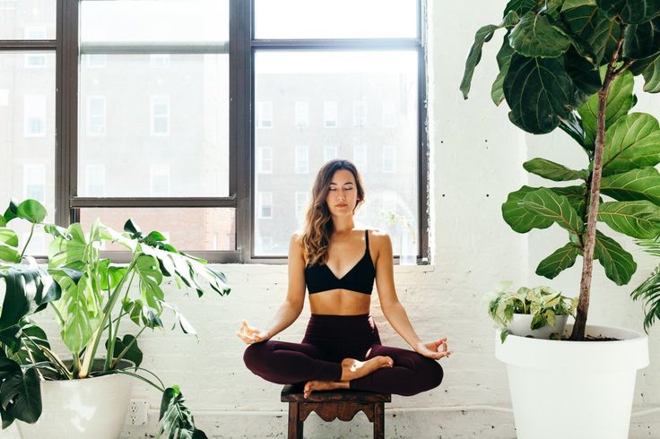 a woman sitting in a yoga pose next to a potted plant