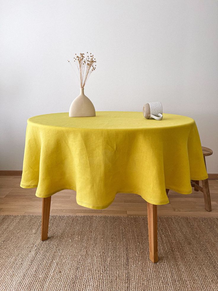 a table with a yellow cloth on it and a white vase sitting on top of it