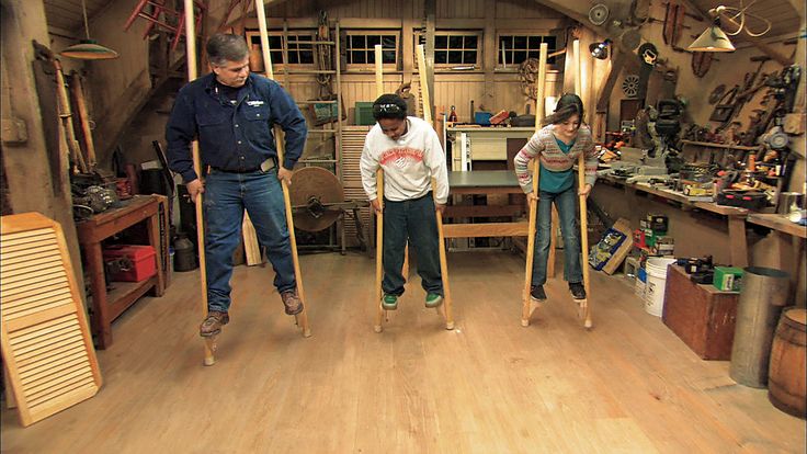 three people standing in a room with wooden flooring and various tools on the walls