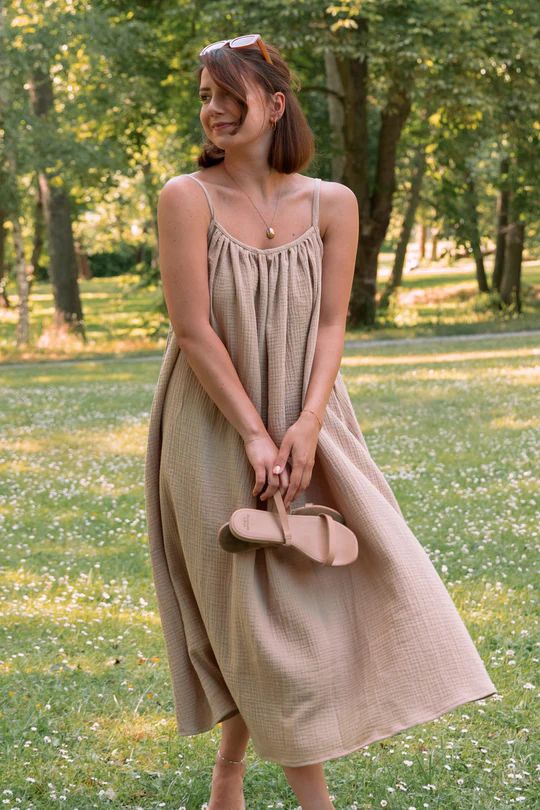 a woman standing in the grass holding a purse