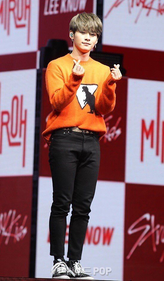 a young man standing on top of a stage wearing an orange shirt and black pants