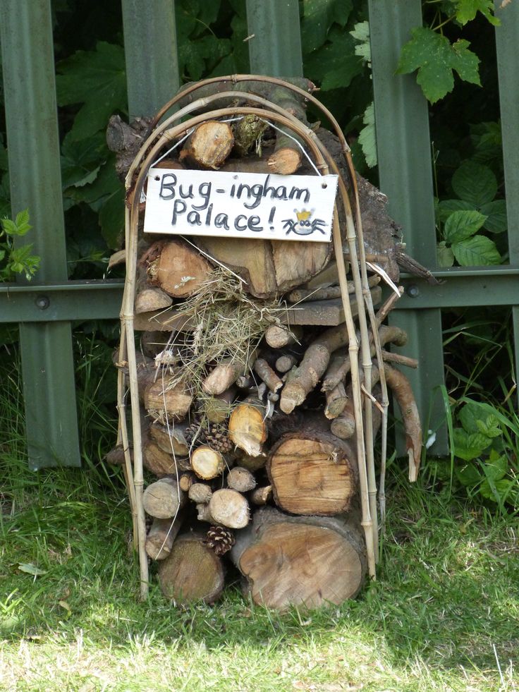 a pile of logs sitting in front of a green fence with a sign on it