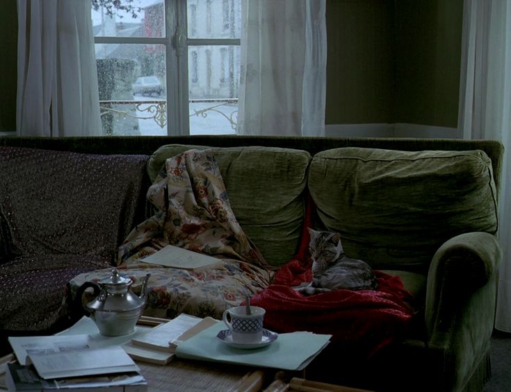 a green couch sitting in front of a window next to a table with books on it