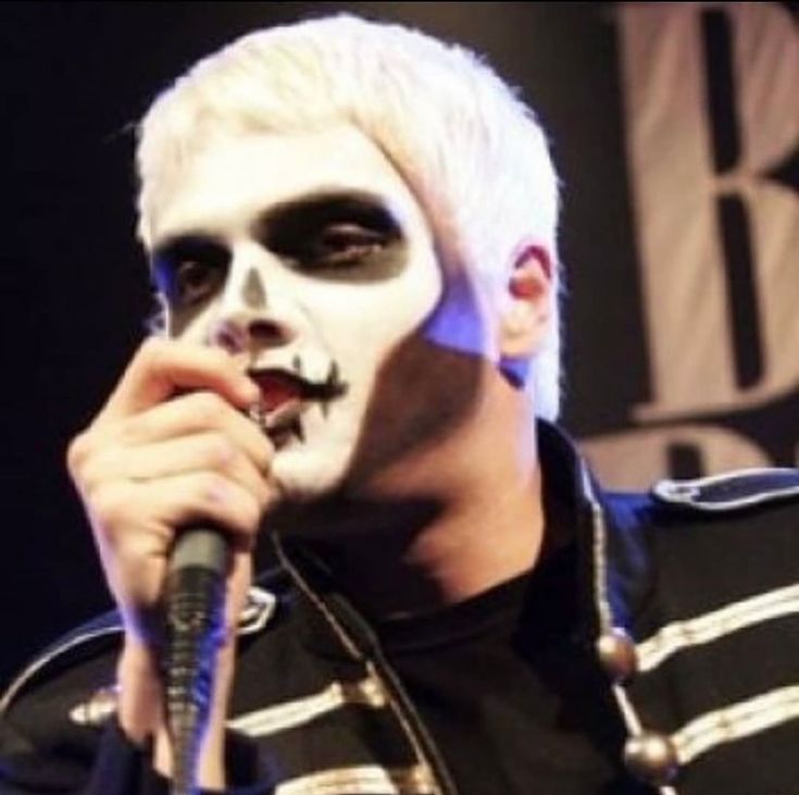 a man with white hair and black face paint holding a microphone