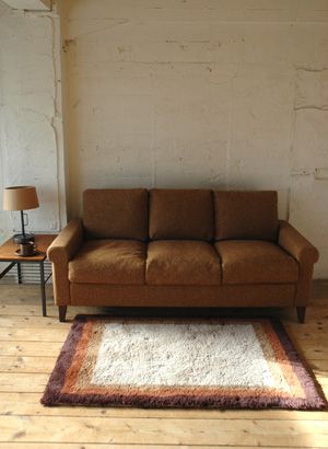 a brown couch sitting on top of a wooden floor next to a lamp and table