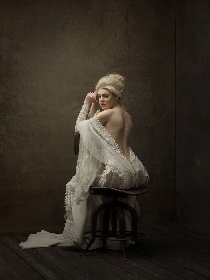 a woman sitting on top of a stool wearing a white dress and holding her hand up to her face