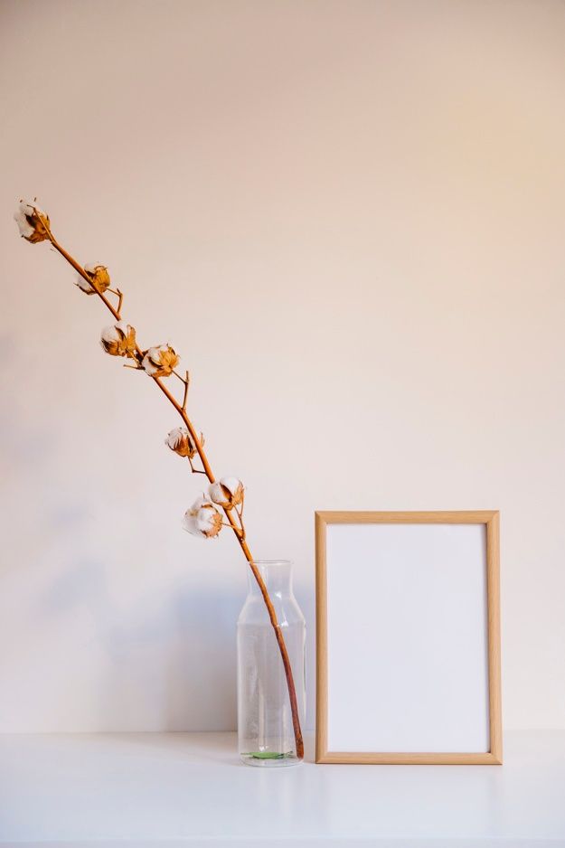 a vase with flowers and a blank photo frame on a white shelf next to it