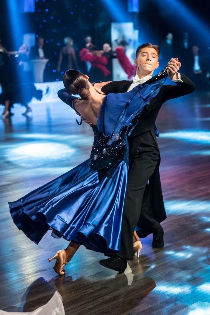 two people dancing on a dance floor with lights in the background and one person wearing a blue dress