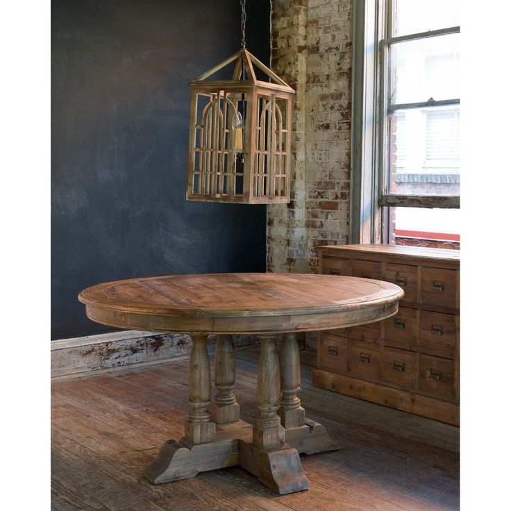 a wooden table with a birdcage hanging from it's center and an old brick wall in the background