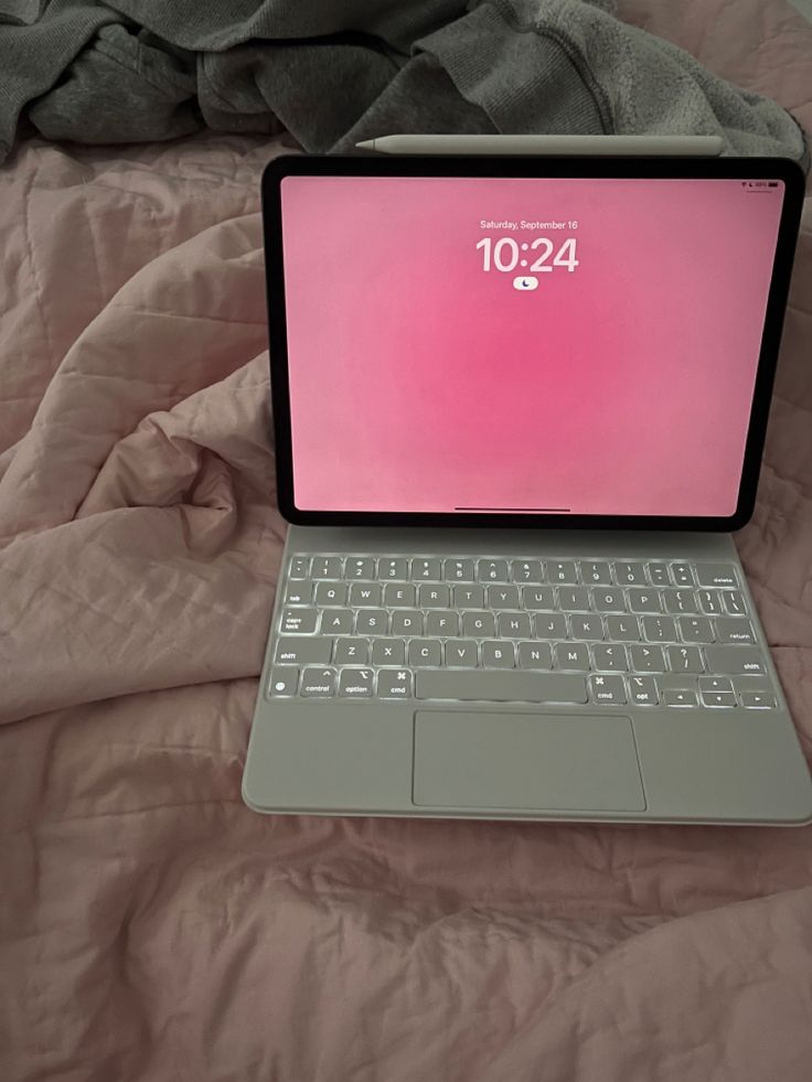 an open laptop computer sitting on top of a pink bed cover covered in sheets and blankets