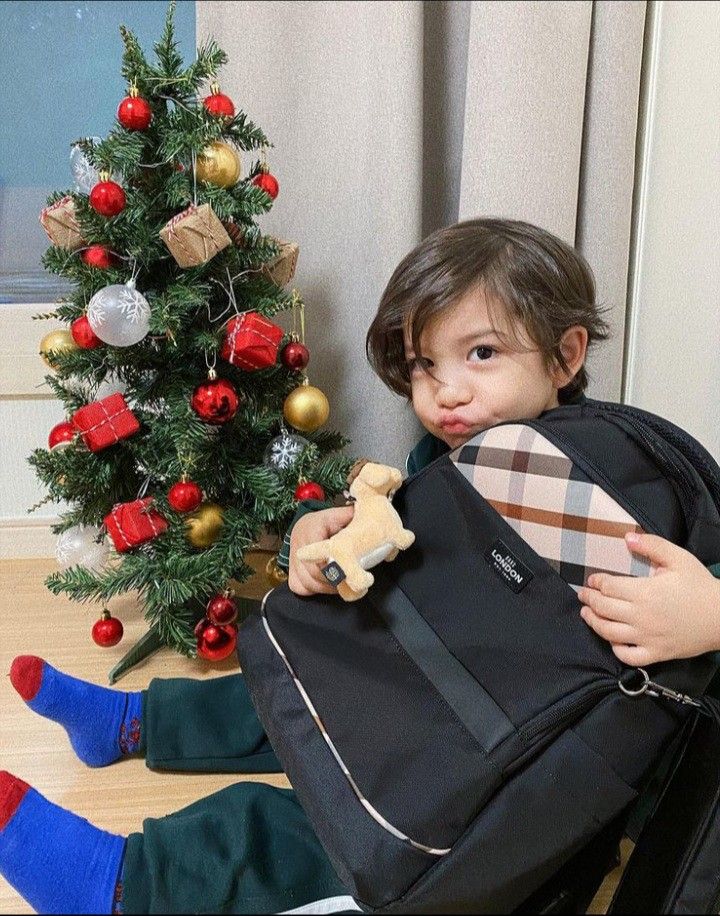 a young boy sitting on the floor with his back pack in front of a christmas tree